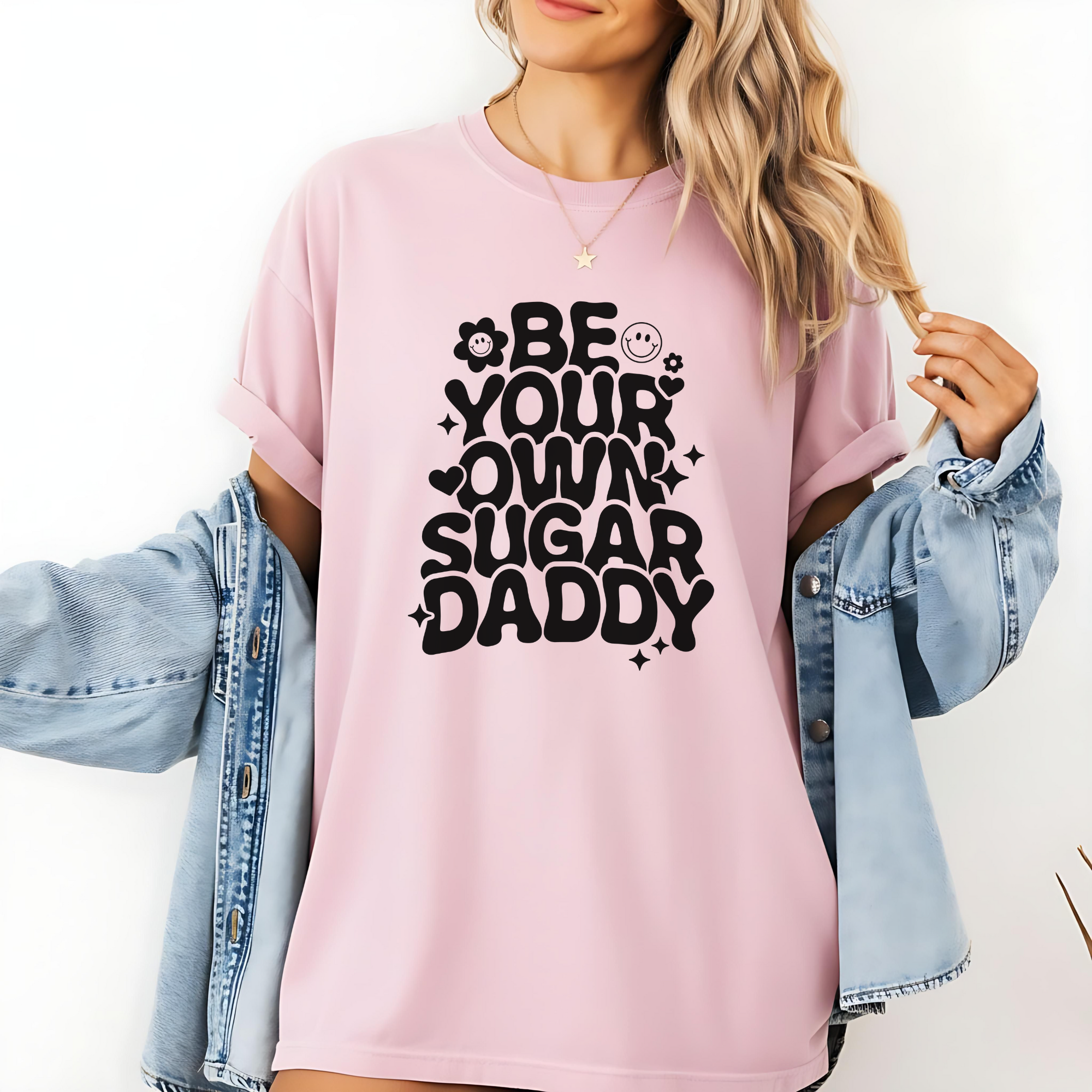 Person wearing a pink t-shirt with 'Be Your Own Sugar Daddy' text design.