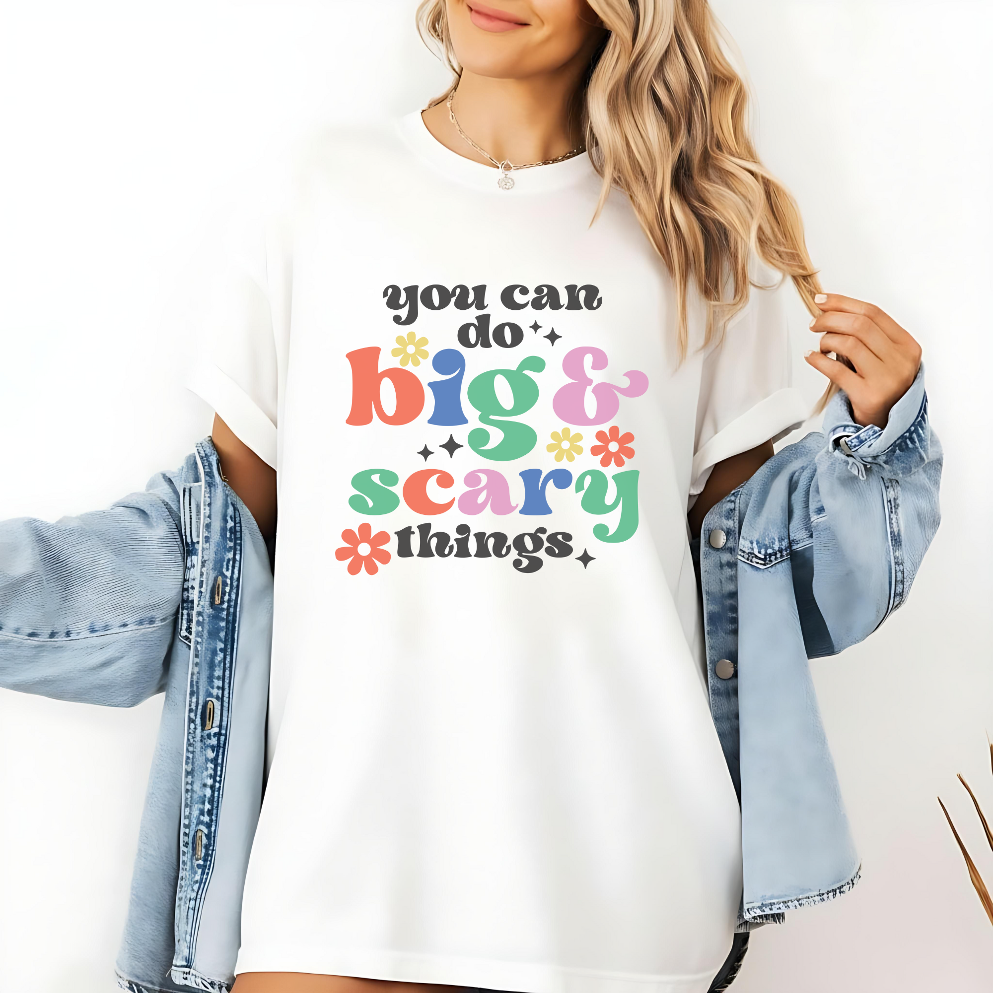 Person wearing a white t-shirt with colorful text 'you can do big & scary things' and a denim jacket.