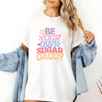 Person wearing a white sweatshirt with colorful text 'Be Your Own Sugar Daddy' and a denim jacket.